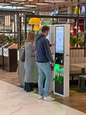 Prague, Czech Republic - March 17, 2026: People using digital self-service kiosks at a fast food restaurant. Modern touch screen ordering and payment.