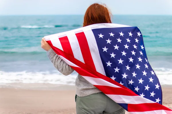 Widok z tyłu młodej dziewczyny z amerykańską flagą patrzy na morze. Święto flagi Ameryki — Zdjęcie stockowe