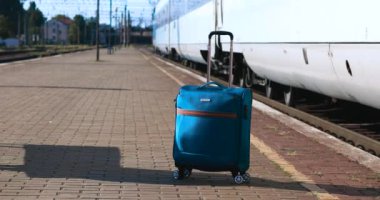 Tren istasyonunda mavi bir valiz duruyor. Yüksek hızlı tren platformdan ayrılıyor. Seyahat ve tatil kavramı