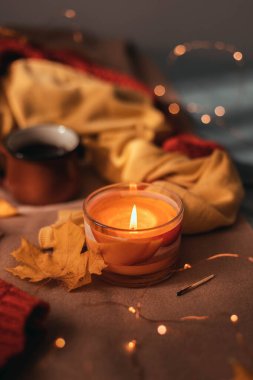 Sonbahar yapraklarıyla yanan aroma mumu ve yatakta kahverengi bir ekose üzerinde hafif çelenk. Sonbahar tarzı. Hygge konsepti, dikey fotoğraf yönelimi