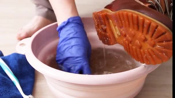 Cleaning shoes. Female hands wash dirty shoes from dirt in a pink plastic basin — Stock Video