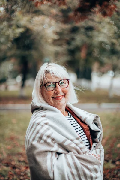 Lycklig kvinna som täcker sig med en varm filt och står i skogen eller parken — Stockfoto