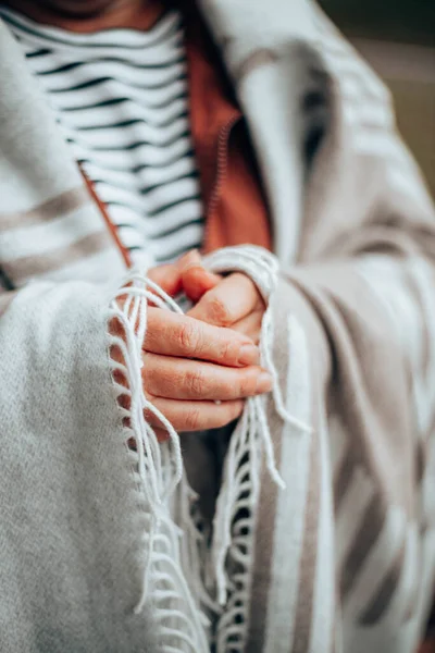 Womens hands in a warm knitted blanket to keep warm in cold October weather in the forest or park