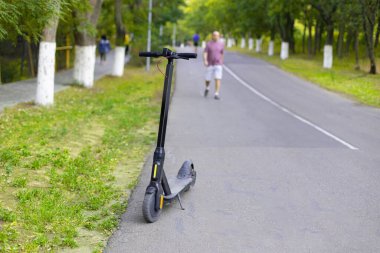 Güneşli bir yaz gününde siyah elektrikli scooter parkın yolu boyunca park edilir. Eko taşımacılığı.