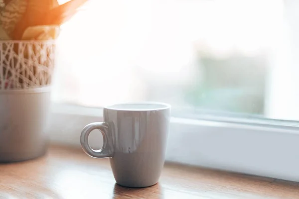 Buenos días, concepto de despertar. Una taza de café aromático o té en un alféizar de madera junto a la ventana. Flor verde en el fondo — Foto de Stock