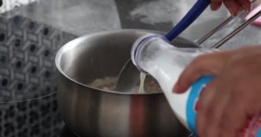 Kadın eli plastik şişeden kepçeye süt döker. Mandıra yulaf lapası pişirmek, güveçte güveç pişirmek.