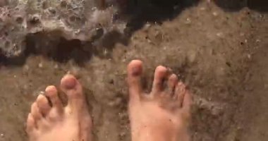 Güneşli bir günde kumların üzerinde çıplak ayaklı bir kadın. Deniz suyuyla kumsalda yürüyen kız bacağı. Köpüklü su dalgası.