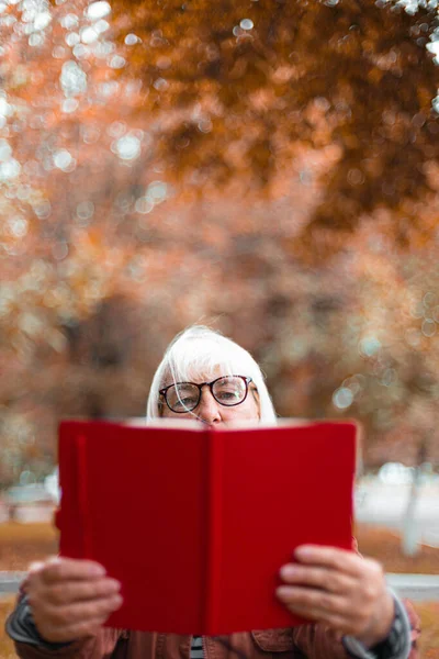 Closeup de uma mulher de óculos e roupas casuais está lendo um livro enquanto relaxa no parque — Fotografia de Stock