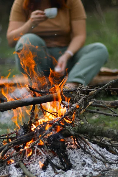 Bonfire in spring forest. Fire coal forest. Young girl drinking a hot drink in the background, shallow depth of field — Stock Photo, Image