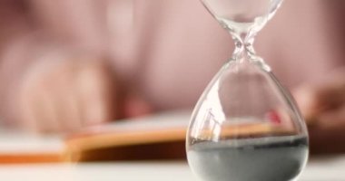 Kum saatinde kum akıyor. Öğrenci kız bir kitap okuyor, uzaktan çalışma..