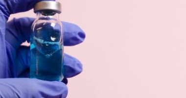 Bir salgın sırasında aşı geliştirme. Tıbbi koruyucu eldivenler içinde doktor eli aşının sıvı şişesini pembe arka planda tutuyor..