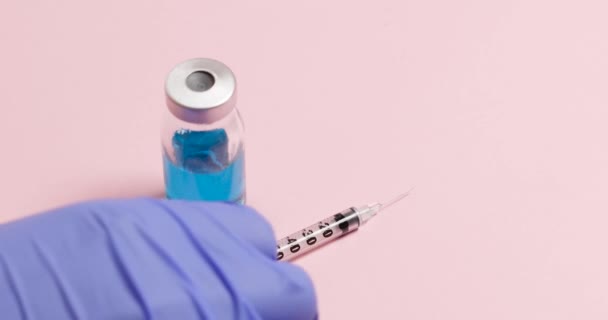 Un médico o enfermero con guantes azules toma una vacuna y una jeringa médica de una mesa para adultos para inyectar durante una pandemia. — Vídeos de Stock