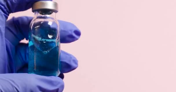 Impfstoffentwicklung während einer Pandemie. Ärztin mit medizinischen Schutzhandschuhen hält die Impfflüssigkeitsflasche vor rosa Hintergrund. — Stockvideo