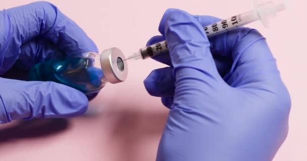 Lekarz ręka w rękawiczce trzymać szklaną butelkę leku z płynną szczepionką dla dzieci i osób szczepionych na różowym tle. — Wideo stockowe