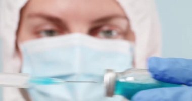 Koruyucu giysili ve koruyucu eldivenli beyaz bir doktor bir koronavirüs aşısı ampulü tutuyor. Şırınga iğnesi için bir şişe.