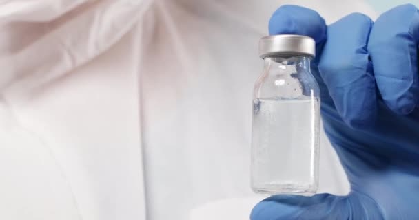 Ученый в синих нитрильных перчатках держит грипп, корь, коронавирусную бутылку вакцины в лаборатории — стоковое видео