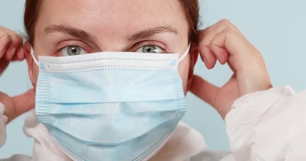 De arts draagt persoonlijke beschermingsmiddelen tijdens de coronaviruspandemie. Vrouw zet medische chirurgische masker of respirator op haar gezicht om te beschermen tegen influenza, mazelen of covid 19 infectie — Stockvideo