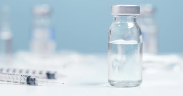 El médico o científico en guantes protectores de goma azul toma un frasco con un líquido de vacuna transparente. Una jeringa de insulina con una aguja yace sobre la mesa — Vídeos de Stock