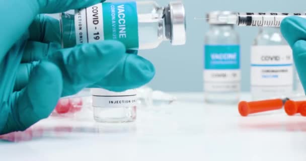 Коронавирус. Лекарственная вакцина Covid-19 в стеклянном флаконе с прозрачной жидкостью в руках врачей в лаборатории. Шприцы с иглой для инъекций и массовой вакцинации. Здравоохранение — стоковое видео
