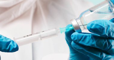 Doktor mavi tıbbi eldivenlerle şeffaf sıvı koronavirüs aşısı şişesini ve şırıngayı laboratuara gönderdi. Hastalıklar için yeni tedavi araştırmaları ve geliştirmeleri