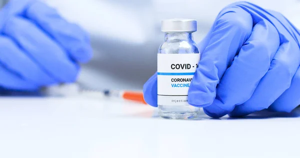 Corona virus Vaccine concept, doctor hands in blue medical gloves with transparent liquid coronavirus vaccine bottle and syringe for injection in the laboratory. Research and development of new cure for diseases