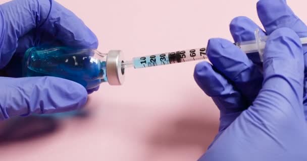 Medizinische Hände halten Spritze und Glasflasche mit flüssigem Impfstoff auf rosa Hintergrund. Entwicklung, Entstehung, Coronavirus, Impfstoff, COVID-19 — Stockvideo