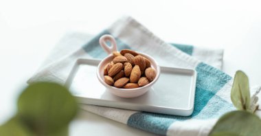 Beyaz arka planda havluyla seramik bir kasede taze fındık bademi. Ön planda yeşil bitki