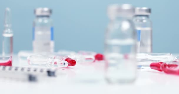 Close-up van griep-, hevige of mazelenvaccin vloeibare fles op medische tafel in het laboratorium, verschillende medicijnen en spuiten liggen op een witte achtergrond. Gezondheidsconcept — Stockvideo