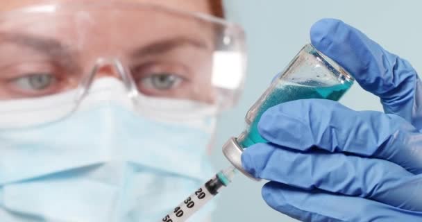 医師または看護師の保護医療用外科用マスクおよびスーツには、ガラスCOVID-19コロナウイルスワクチンアンプル、実験室または実験室で注射器付きボトルが収納されています。 — ストック動画