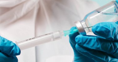 Lateks mavi eldivenli doktor ya da hemşire elinde şırınga ve Covid-19 Coronavirus aşı şişesi tutuyor.