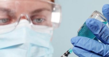 Koruyucu tıbbi maske takan bilim adamı ve grip, kızamık, koronavirüs aşısı tutan mavi azot eldivenleri. Doktor, yetişkinlerin ve çocukların rutin aşılanması için sıvı içeren bir şırınga tutuyor.