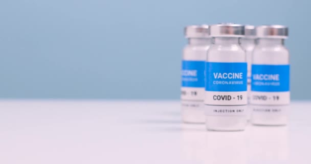 Vacunación contra el coronovirus de la población. SARS-CoV-2 frasco de vidrio de vacuna y jeringa en una mesa de laboratorio blanca con espacio para copias. Movimiento suave de la cámara — Vídeo de stock