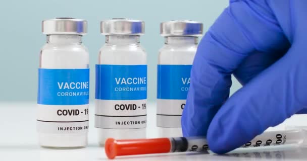 Ręce lekarza w niebieskich rękawiczkach medycznych z przezroczystą, płynną butelką zawierającą szczepionkę koronawirusową i strzykawką do wstrzykiwań w laboratorium. — Wideo stockowe