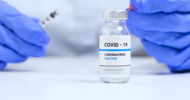 La doctora pone las manos en guantes médicos azules con frasco transparente de vacuna contra el coronavirus líquido y jeringa para inyección en el laboratorio. Investigación y desarrollo de una nueva cura para las enfermedades — Vídeos de Stock