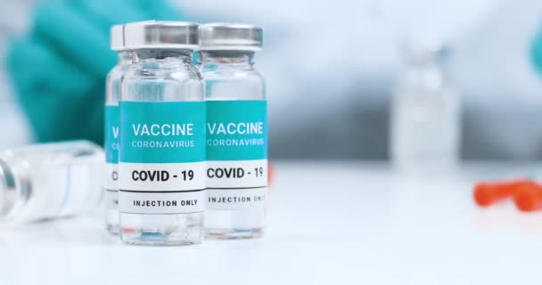 Doktor Coronavirus aşısı için bir şırınga aldı. Aşı şişeleri beyaz laboratuvar masasında. Genel Aşılama. — Stok video