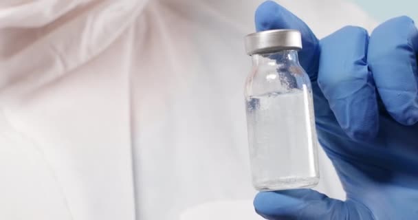 Ученый в синих нитрильных перчатках держит вакцину от гриппа, кори, коронавируса. Разработка и создание коронавирусной вакцины COVID-19. — стоковое видео