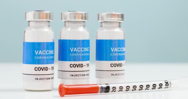 Coronovirus, covid-19 vaccinatie van de populatie. Vaccin injectieflacons en spuit op een witte laboratoriumtafel met copyspace. Gezondheidszorg kuur concept — Stockvideo