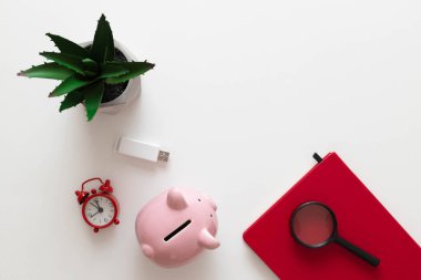 Serbest ofis iş yeri konsepti. Kırmızı defter, doğa santrali, alarm saati ve beyaz minimalist arka planda fotokopi alanı olan kalemler. En az çalışma alanı
