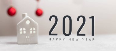 2021 Mutlu Yıllar kompozisyonu. Küçük oyuncak model ev ve beyaz yatay arkaplanda kırmızı toplar.
