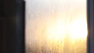 Parlak günbatımı ışığı, ahşap balkon çerçeveli eski bir pencereden girer.