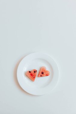 Beyaz arka planda beyaz bir plaka üzerinde kalp şeklinde karpuz 2 dilimleri, dikey yönelim
