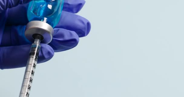 Врач рука в латексных синих защитных перчатках держит шприц и голубую жидкость вакцины или другое лекарство на синем фоне — стоковое видео