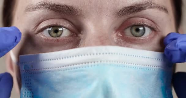 年轻的女医生摘下她的防护口罩，靠近点。COVID-19 Sars-cov-2大流行病 — 图库视频影像