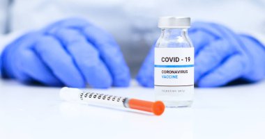 Kadın doktor mavi tıbbi eldivenlerle şeffaf sıvı koronavirüs aşısı şişesi ve şırıngayı laboratuara gönderdi. Hastalıklar için yeni tedavi araştırmaları ve geliştirmeleri