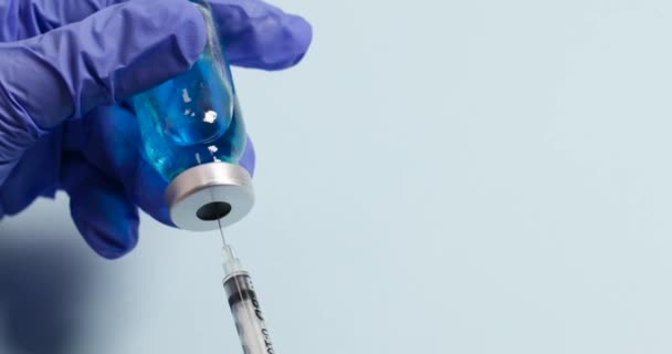 Lékaři rukou v rukavici podržte skleněnou lahvičku s injekční stříkačkou na modrém pozadí. Koncepce vakcíny proti viru Corona 2019-nCoV nebo COVID-19. — Stock video