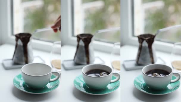 Fehér női kéz forró fekete kávét önt a Cezve kerámia fehér csészéjébe. Reggeli hangulatos reggeli. Videó függőleges történet készlet — Stock videók