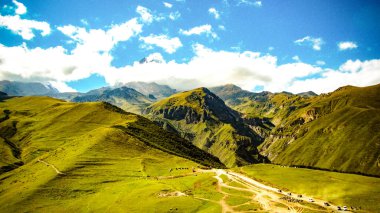 Kazbek Dağı manzarası. Güneşli bir yaz gününde Gürcistan 'ın yeşil dalgalı doğal dağ tepelerinde güzel bir panorama balı