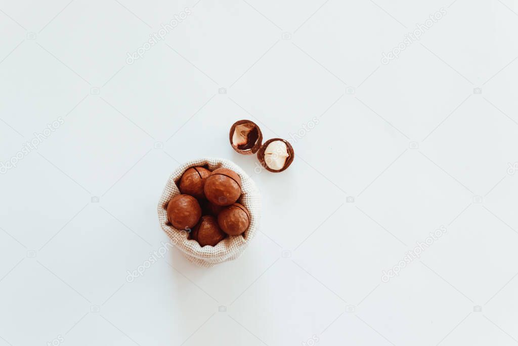 Raw macadamia nuts in canvas bowl on a white solid background. Minimal composition.