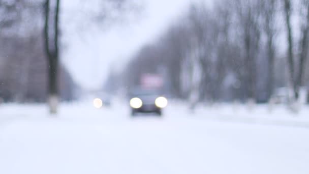 Niewyraźne samochody jadące po drodze pokryte śniegiem na ulicy podczas śnieżnej pogody. Malowniczy widok na ośnieżoną lodową drogę. Opady śniegu zimą — Wideo stockowe