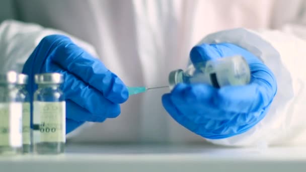 Médico o enfermero manos en guantes de protección médica recoge la vacuna de un vial de vidrio para una inyección contra el coronavirus, el sarampión o la gripe — Vídeos de Stock